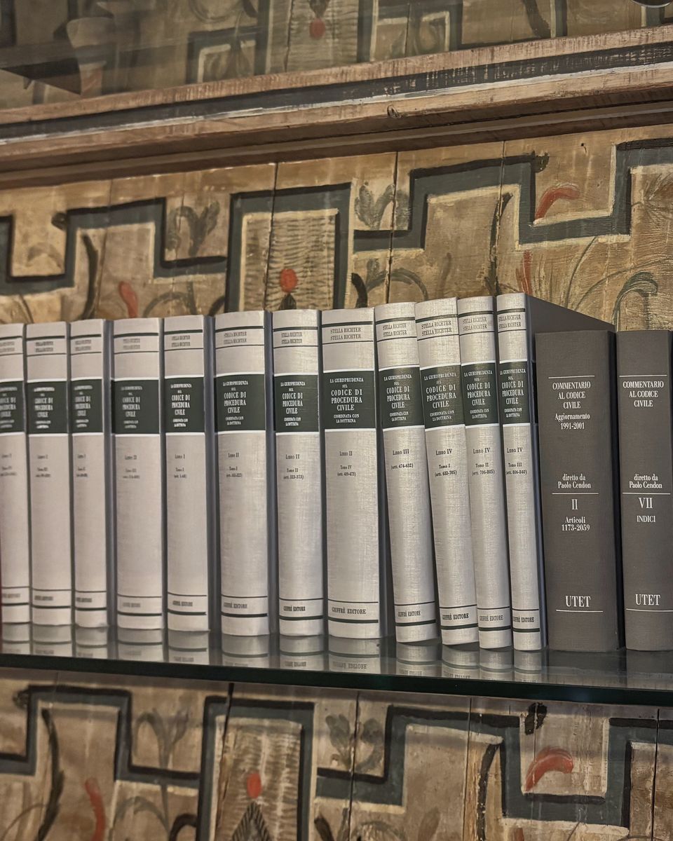 I volumi di giurisprudenza e i commentari sulle mensole in vetro, davanti alla boiserie in legno dipinto dello studio